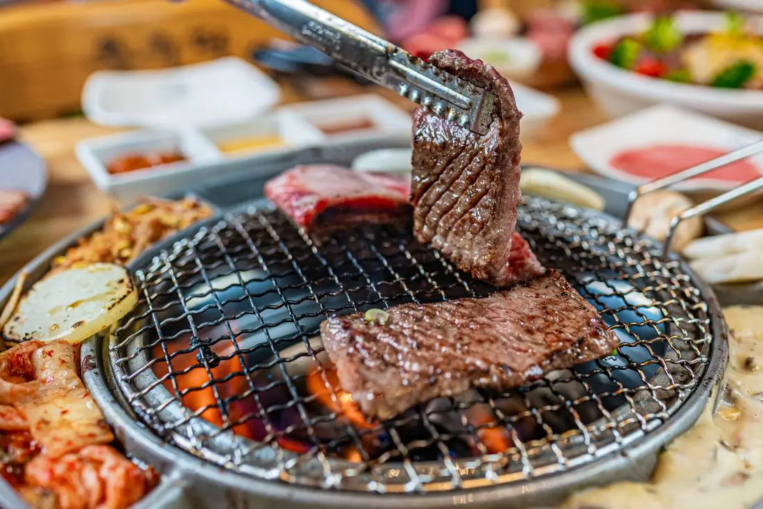Korean barbecue meat lifted with tongs over a charcoal grill